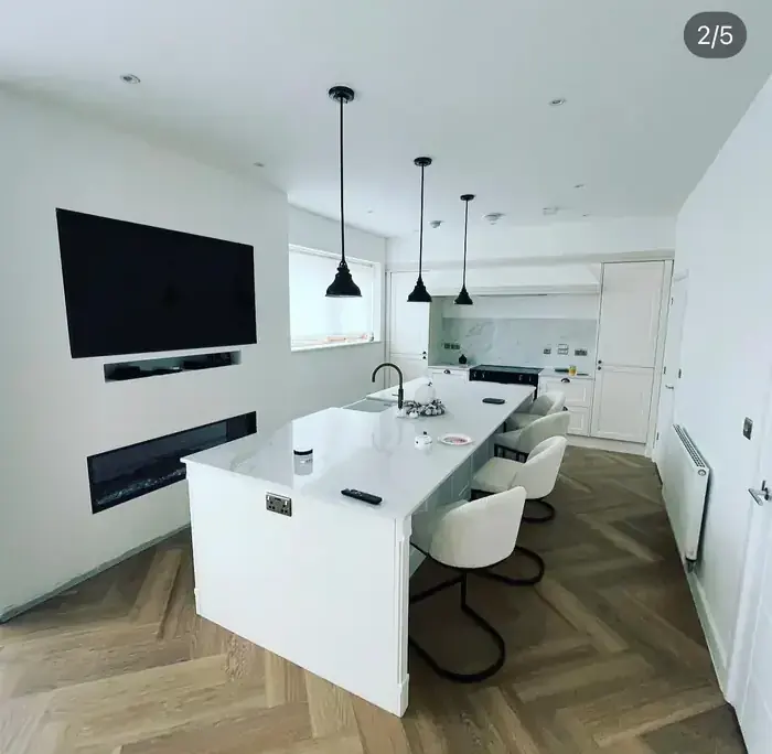 Open-plan living room with fitted joinery, herringbone flooring and a wall-mounted TV recess